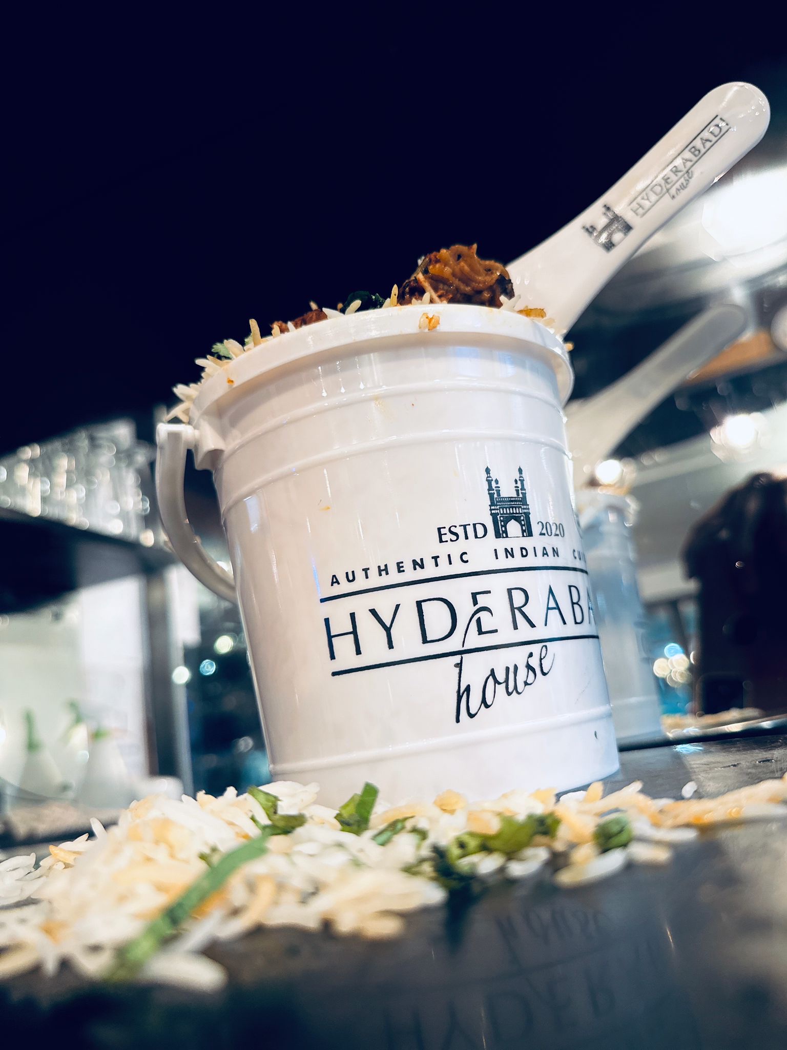Hyderabadi dum biryani in a Hyderabadi House takeaway pot, rice scattered on the counter